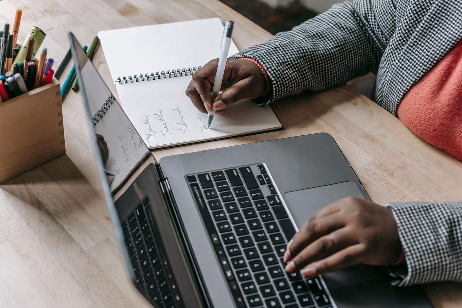 Hands writing in a notebook beside a laptop.